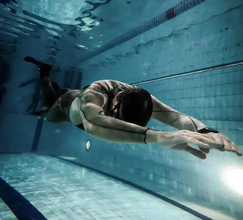 Apnéiste du club en immersion dans la piscine, bras tendus vers l'avant, glissant sous la ligne d'eau